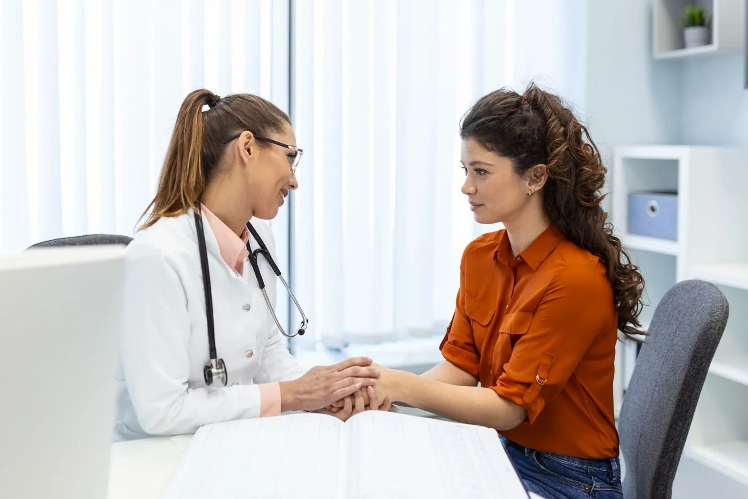 Female doctor holding patient’s hands and offering support during a medical consultation in a clinic.